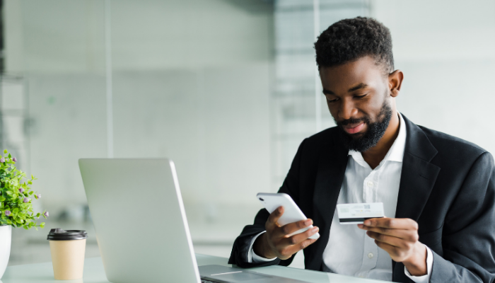 man looking holding a debit card while using a phone